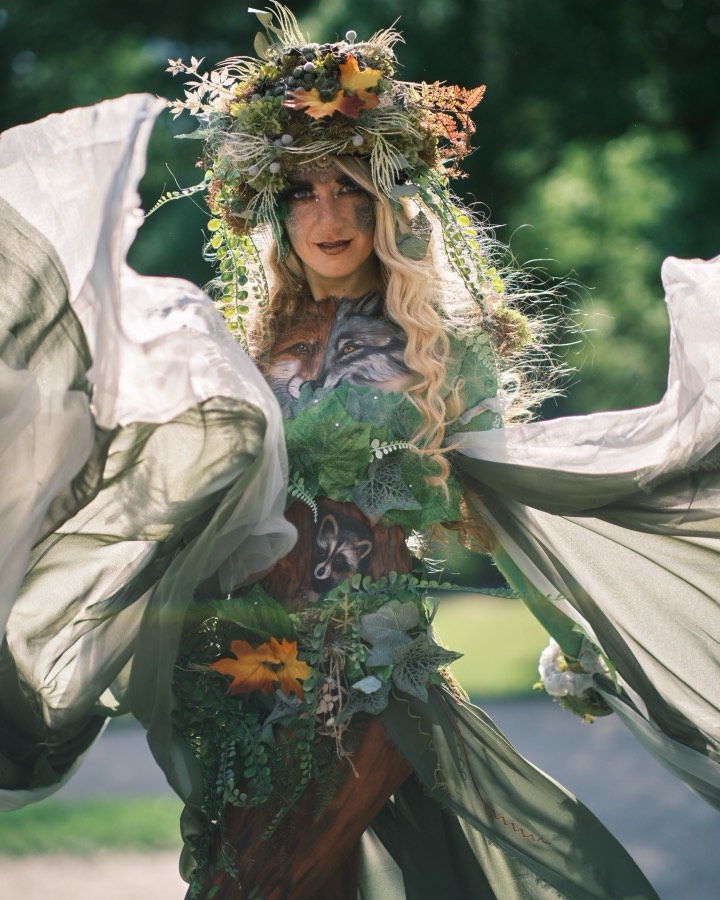 Bodypainting – postava v kostýmu z bílé látky s květinovou korunou a malbou po celém těle